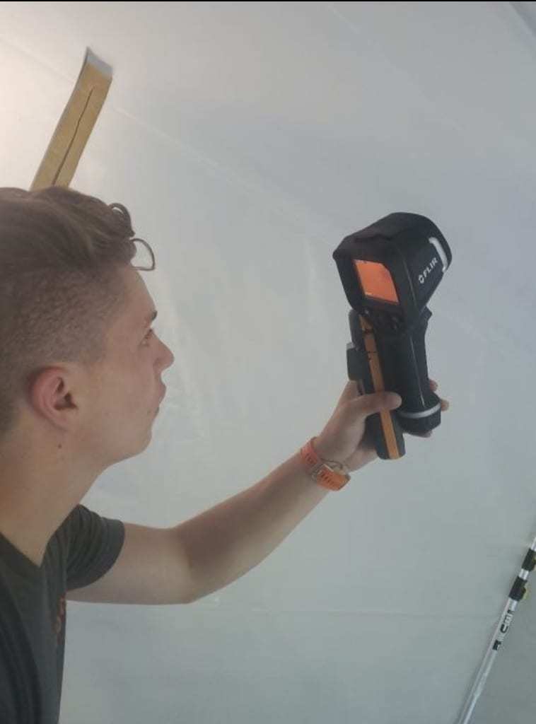 Technician scanning a plastic-covered wall with a thermal camera